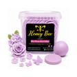 A clear plastic tub filled with lavender-colored wax melts, shown with a black front label reading Honey Bee Lifestyle. Surrounding the tub are lavender wax flower and butterfly ornaments, a lavender wax ball, and a round lavender wax disc, all on a white background.