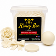 A clear plastic tub filled with cream-colored wax melts or beeswax products, with a black and yellow Honey Bee label. Surrounding the tub are decorative wax melts shaped like a rose, flower, bow, and a round disc, all on a clean white background.