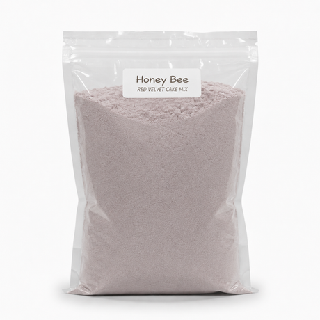 A clear resealable stand-up pouch filled with a pale pink cake mix, labeled 'Honey Bee Red Velvet Cake Mix' on a white background.