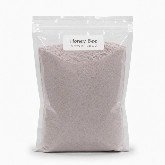 A clear resealable stand-up pouch filled with a pale pink cake mix, labeled 'Honey Bee Red Velvet Cake Mix' on a white background.